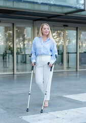 business blonde woman walking with two crutches in front of an office building