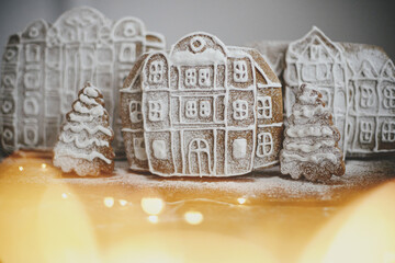 Christmas gingerbread houses and tree in snow on rustic wooden table with golden lights. Christmas cookies village scene. Atmospheric moody image. Winter holiday traditions. Merry Christmas!