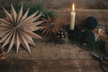 Stylish Christmas paper stars, candle, ornaments, pine cone on rustic wooden background. Xmas...