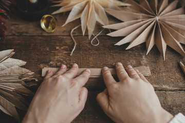 Making stylish Christmas stars. Hands folding craft paper on background of handmade sweden stars,...