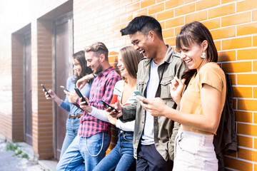 Multicultural friends laughing using smartphone at wall on university college campus - Young people addicted by mobile smart phones - Technology concept with always connected - bright filter