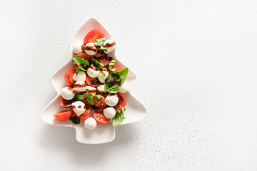 Festive caprese salad of tomatoes, mozzarella cheese for Xmas party in plate as Christmas tree on white background. View from above. Copy space.