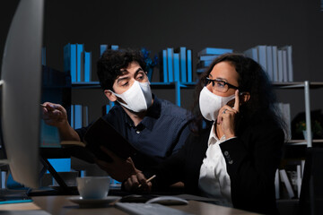 2 business men and women, financial staff  marketing staff   working at night, wearing a mask.  Preventing Covid 19
