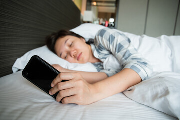 Lazy Asian young woman trying to snooze awaking alarm clock in smartphone.