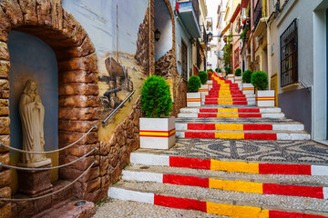 Narrow alley decorated with the flag of Spain on the steps. Calpe Alicante. - obrazy, fototapety, plakaty