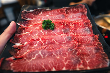 Sliced beef shabu in a black plate in a restaurant