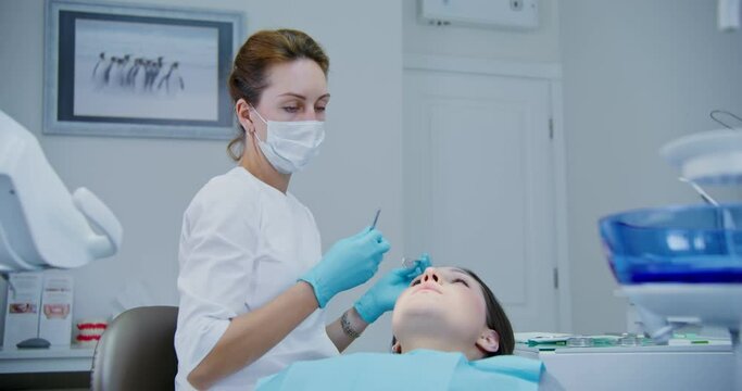 The dentist takes a medical instrument and begins an examination of patient's