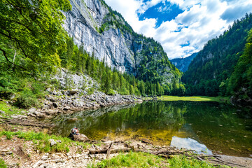 Hikers sitting on a rock at the lakeshore of Lake Kammersee, Ausseer Land, Styria, Austria, which is enclosed by mountains and a primeval forest