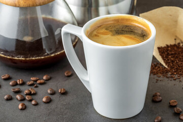 A cup of coffee and third generation pour over coffee brewing equipment on stone floor