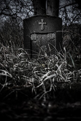 A derelict stone tombstone with a cross in an abandoned cemetery
