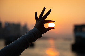 female Hand or fingers hold the warm rays of sunshine or sun during sunset