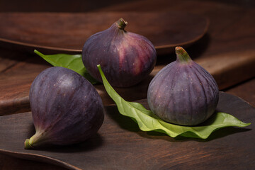 A fresh figs with green leaves on a wooden plate. Ripe delicious figs whole on rustic background. A Food Photo. Selective focus.