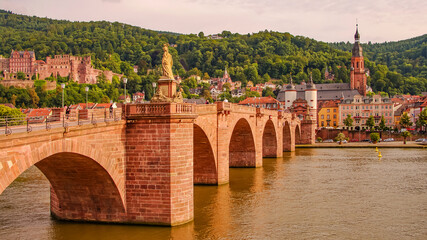 Fototapeta na wymiar Stunning reddish sunset over the old historical downtown, castle as a city fortress, and main city bridge with a medieval city gate over Neckar river in Heidelberg, Germany.