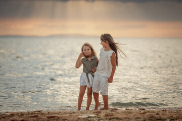 Two sisters playing on the shore of the sea at summer evening