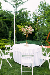 Table with bouquet and chairs around it are on at wedding banquet in lawn at garden.
