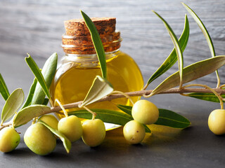 Close-up of an olive tree branch with green olives on the background of a bottle of olive oil.