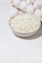bowl of fresh farm cottage cheese and eggs on a white background, vertical top view