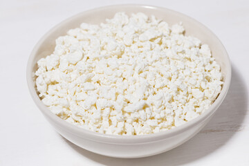 bowl of fresh farm cottage cheese on a white background, closeup