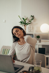 Beautiful woman having back and neck pain while using a laptop at home