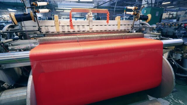 Colourful fabric is getting woven by factory machinery