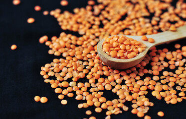 A wooden spoon with lentils on a dark surface surrounded by lots of lentils.