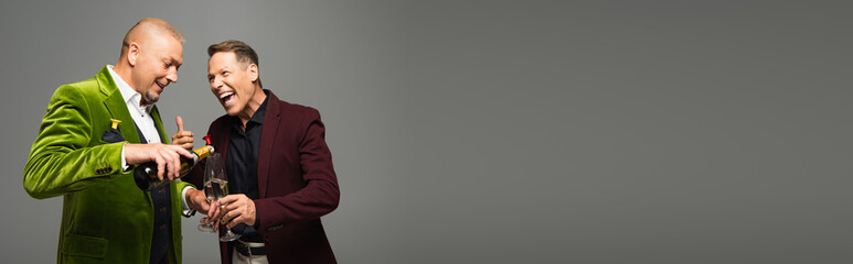 Positive mature man showing like while friend pouring champagne isolated on grey, banner