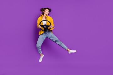 Fototapeta na wymiar Photo of impressed funny young woman dressed yellow shirt smiling jumping high holding steering wheel isolated purple color background