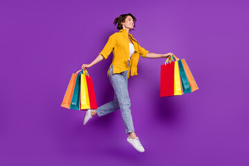 Photo of funky pretty young lady wear yellow shirt jumping high holding shopping bags looking empty...