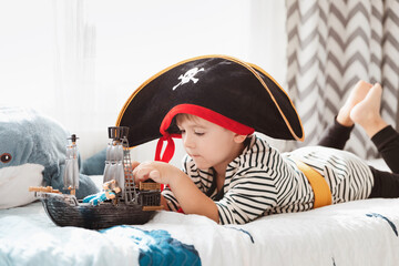 Little child boy in pirate hat and carnival costume playing with pirate ship toy in kid's room.
