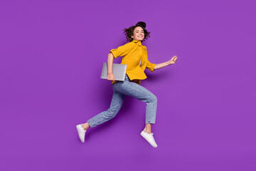 Photo of shiny pretty young woman dressed yellow shirt smiling jumping running holding modern device isolated purple color background