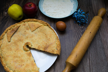 Homemade apple pie next to apples, flour, eggs and a rolling pin on a rustic wooden table