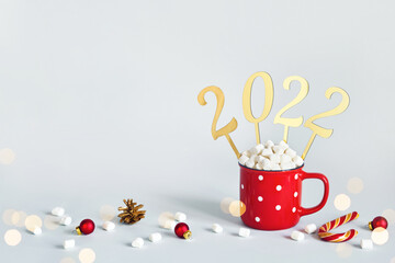 Christmas or New Year 2022 concept. Red mug of cocoa with marshmallows and golden numbers 2022, copy space
