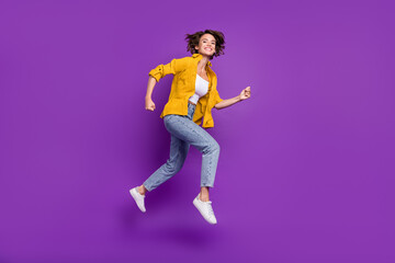 Fototapeta na wymiar Photo of adorable shiny young woman dressed yellow shirt smiling jumping high running fast isolated purple color background