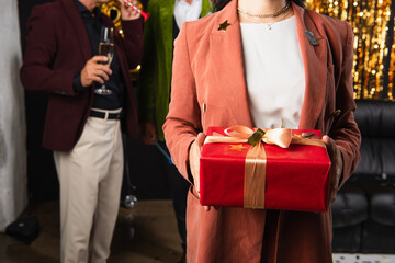 Cropped view of woman holding gift box with confetti near blurred friends on black background