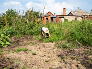 woman in hat weeds garden beds on sunny day