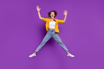 Fototapeta na wymiar Photo of charming funny young lady wear yellow shirt jumping high smiling isolated violet color background