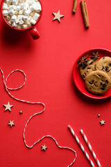 Christmas red table with mug of hot cocoa with marshmallows, oatmeal cookies, cinnamon sticks, ribbon. Flat lay, top view.