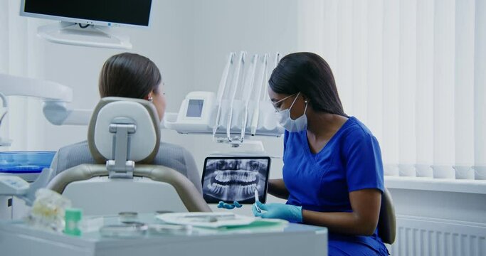 A dentist shows a woman patient a picture of teeth using a tablet