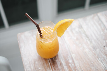 Glass of fresh orange juice and  straw on the wooden table in cafe house.