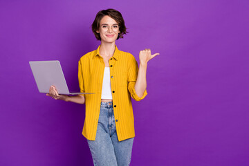 Portrait of attractive trendy cheery girl holding laptop showing copy space isolated over bright violet purple color background