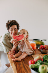 Kid girl with mom eating watermelon. Happy family in the kitchen.  