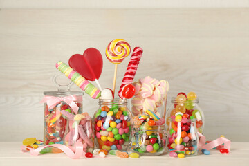 Jars with different delicious candies on beige wooden table