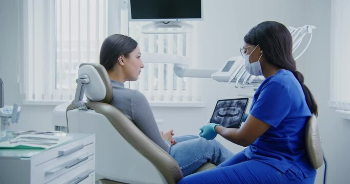 A dentist shows a woman patient a picture of teeth using a tablet