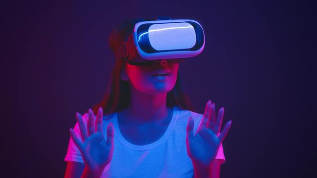 Excited young asian woman wearing vr glasses playing online, touching virtual buttons in neon lights, slow motion