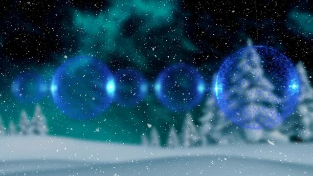 Multiple blue bauble decoration hanging against snow falling over winter landscape