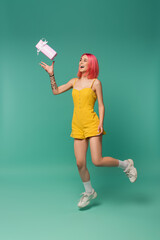 full length of smiling young woman with pink dyed hair jumping and throwing present on blue