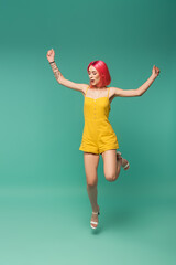 full length of excited young woman with pink dyed hair in romper jumping on blue