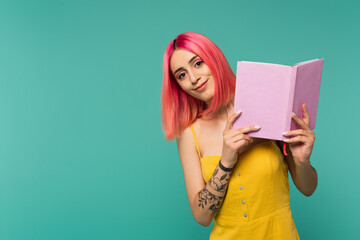 smiling young woman with pink dyed hair holding book isolated on blue