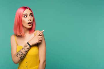 amazed young woman with pink dyed hair poising with finger isolated on turquoise