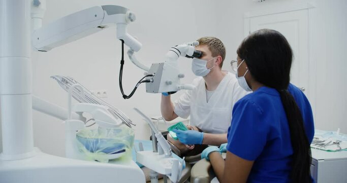 Male dentist looks through dental microscope for patient's tooth root canal
